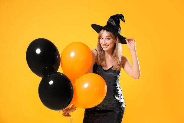 Beautiful woman in witch costume with balloons on yellow background. Halloween party - 写真・画像