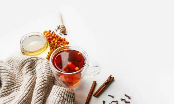 果実、蜂蜜、ローワンと海のクロウメモドキの果実、シナモンスティックとニットベージュのセーターで軽いテーブルの上にドライクローブとビタミン茶。免疫系を強化するのに役立つ製品です - 写真・画像