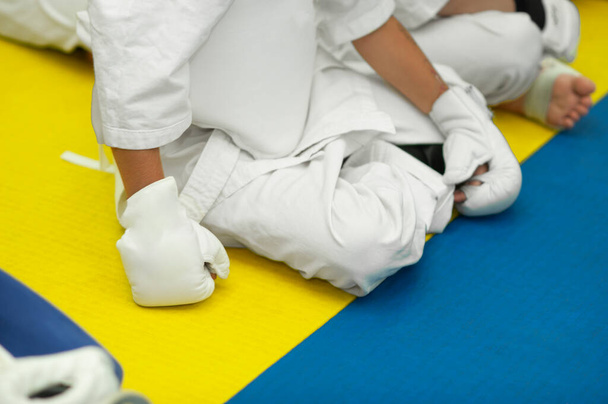 Kind ohne Gesicht in weißem Trainingsanzug und Handschuhen für den Kampf auf blauem und gelbem Tatami - Foto, Bild