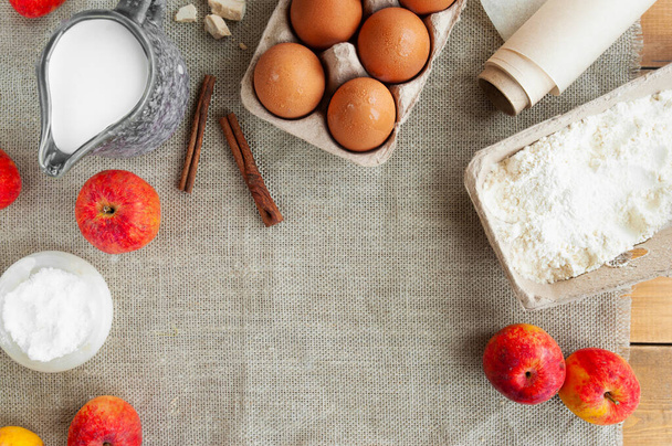 ingredience na jablečný koláč. přísady na pečení na dřevěném stole. hnědá vejce v lepenkové krabici, domácí drcené jablečné mléko ve džbánu, sůl, mouka, droždí a pečivo - Fotografie, Obrázek