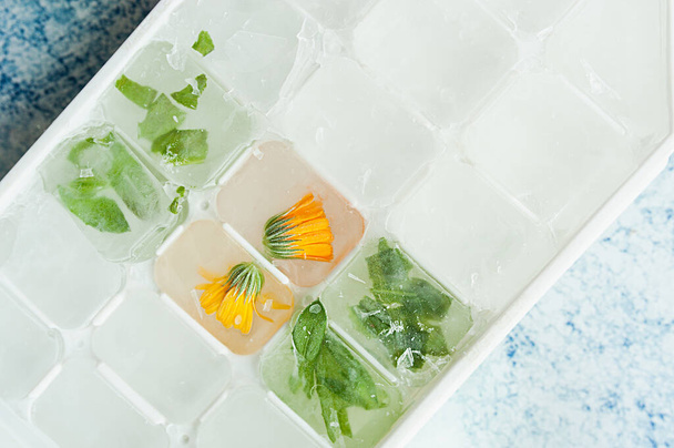 frozen ice cubes with orange calendula flower and green leaves, cosmetic layout, simple skin care - Photo, Image