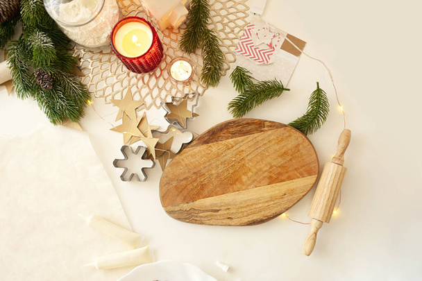 deska do cięcia drewna, mały wałek, gałęzie drzew, płonące świece i metalowe ciasteczka frezy na beżowym lekkim świątecznym stole - Zdjęcie, obraz