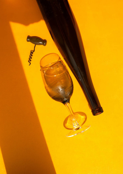 üveg, sötét üveg borosüveg és dugóhúzó élénk sárga alapon természetes fényben kemény árnyékokkal, felülnézet - Fotó, kép
