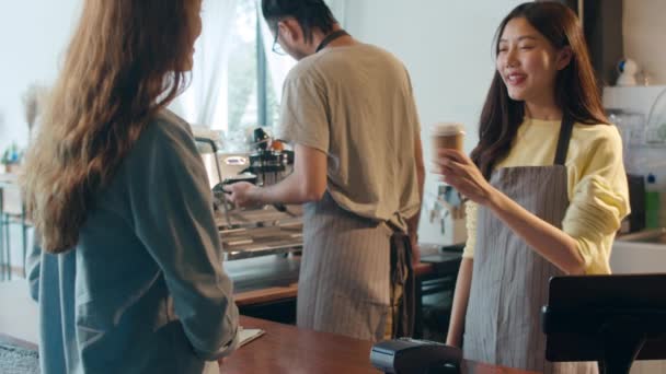 Fiatal ázsiai női barista szolgálja elviszi a forró kávé papír csésze a fogyasztónak, és a hitelkártya fizetési állni pult mögött kávézó étterem. Tulajdonos kisvállalkozás, élelmiszer és ital koncepció - Felvétel, videó