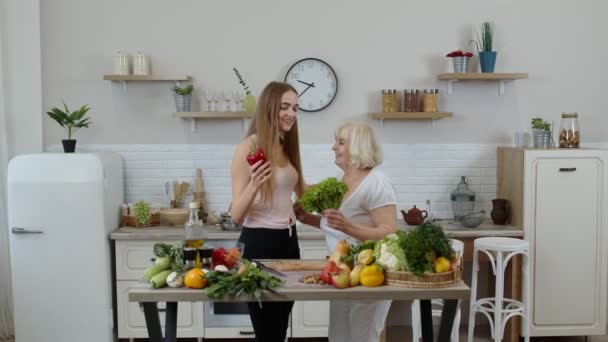 Mujer madura con nieto niña recomendando comer alimentos vegetales crudos. Concepto del día mundial vegano - Imágenes, Vídeo