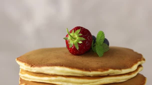 Pancake con fragola, mirtillo e menta in piatto di ceramica ruotato su tavolo leggero, primo piano. - Filmati, video