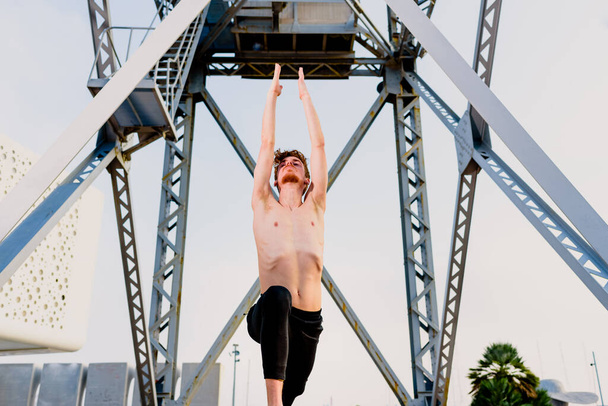Joven realizando ejercicio de movimiento conjunto inspirado en yoga, al aire libre. - Foto, imagen