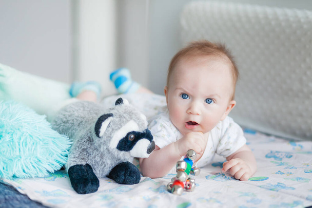 pequeño niño de 3 meses de edad se encuentra boca abajo en el sofá en una habitación luminosa, el niño sonríe, juega con juguetes - Foto, imagen