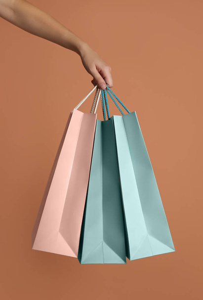 Woman holding paper shopping bags on light brown background, closeup - Foto, afbeelding
