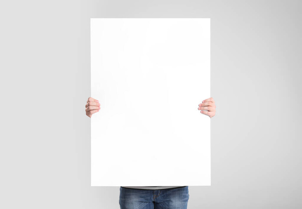 Man holding blank poster on light grey background - Foto, afbeelding
