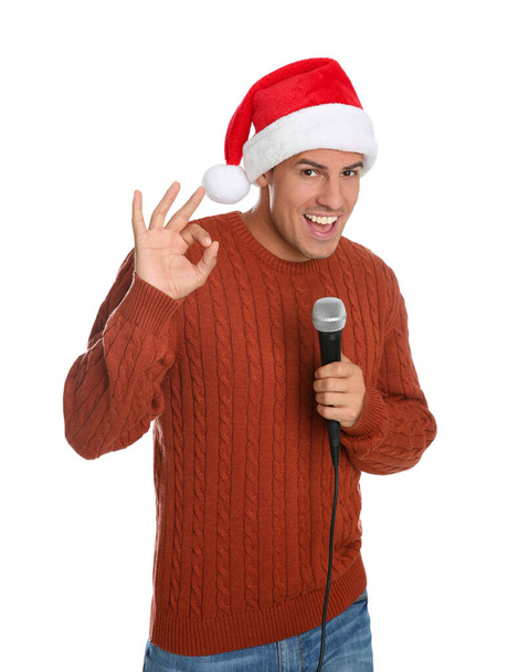 Emotional man in Santa Claus hat singing with microphone on white background. Christmas music - 写真・画像