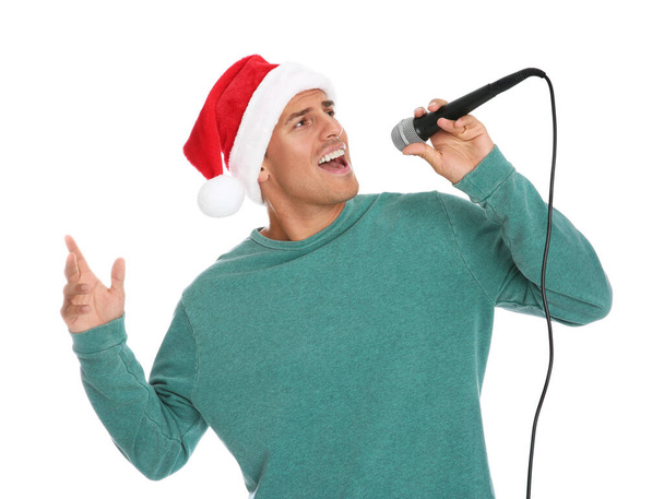 Emotional man in Santa Claus hat singing with microphone on white background. Christmas music - Фото, изображение
