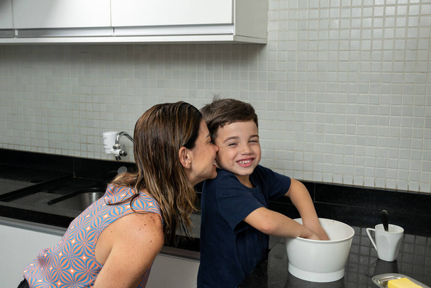 6 Year old boy mixing the cookie dough and his mother kissing him on the cheek. - Photo, Image