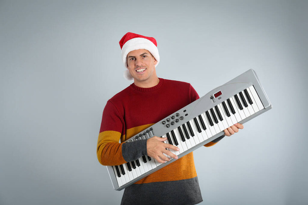 Man in Santa hat playing synthesizer on light grey background. Christmas music - Foto, Bild