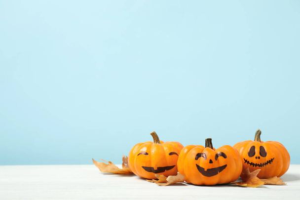 Pumpkins with scary faces and fallen leaves on white wooden table, space for text. Halloween decor - Fotografie, Obrázek