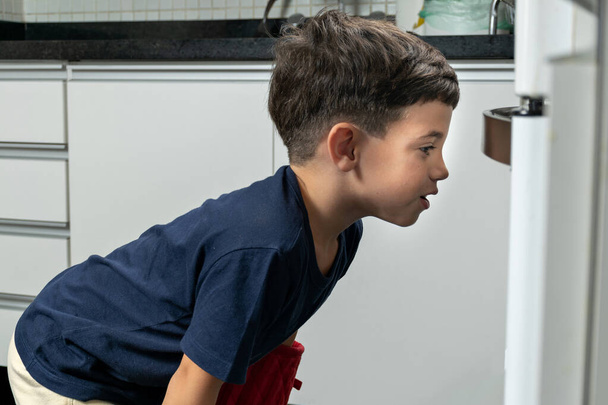 Ребенок с волнением ждет, когда кулич закончит выпечку в духовке. - Фото, изображение