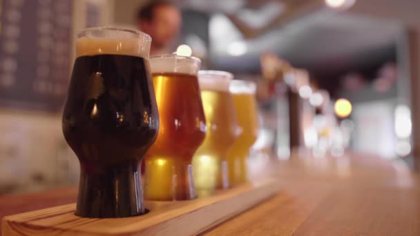 Vasos de cerveza artesanal en un mostrador de bar con barman vertiendo cerveza de barril - Metraje, vídeo