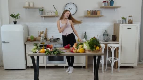 Ευτυχισμένο χορτοφαγικό κορίτσι με λεπτή μέση χορεύει, τραγουδά στην κουζίνα. Έννοια διατροφής ακατέργαστων λαχανικών - Πλάνα, βίντεο