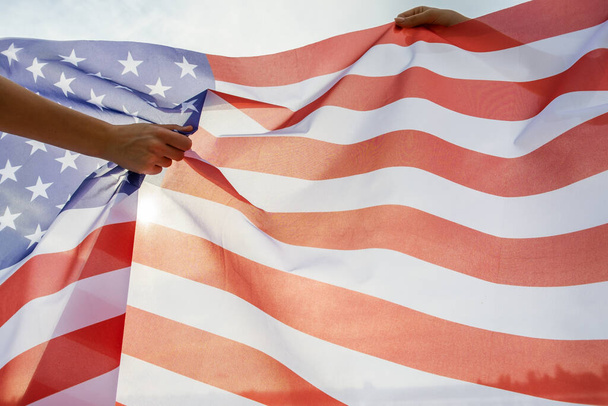Duas mãos humanas segurando a bandeira nacional dos EUA. Celebração do conceito de Dia Internacional da Democracia. - Foto, Imagem