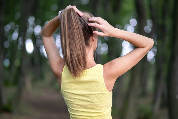 Молода жінка зв'язує її довге волосся, стоячи на відкритому повітрі
. - Фото, зображення