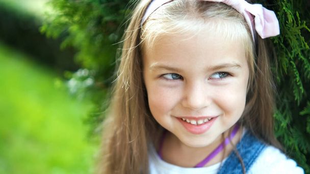 Πορτρέτο του όμορφου μικρού κοριτσιού που στέκεται σε εξωτερικούς χώρους στο καλοκαιρινό πάρκο χαμογελώντας ευτυχισμένοι. - Φωτογραφία, εικόνα