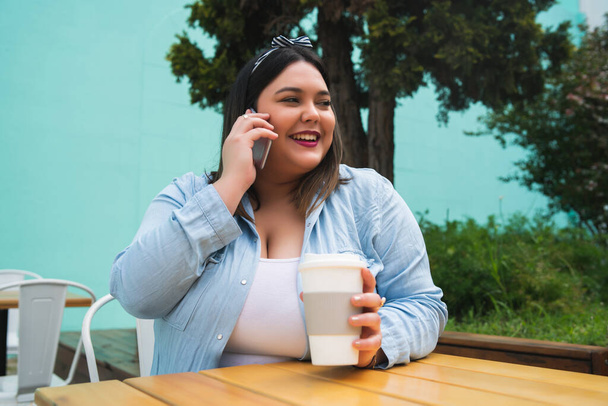 Portrait of young plus size woman talking on the phone while sitting outdoors at coffee shop. - Foto, Bild