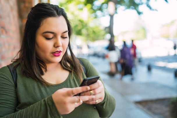 Portrait of young plus size woman typing text message on her mobile phone outdoors at the street. Technology and urban concept. - Fotografie, Obrázek