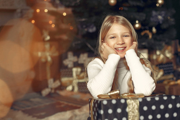Kleines Mädchen im weißen Pullover neben Weihnachtsbaum mit Geschenk - Foto, Bild