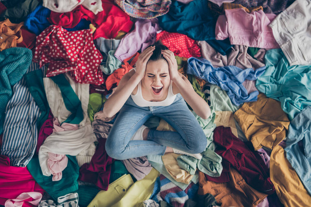 Help. High angle above view photo of stressed yelling lady stay home spring cleaning household sit many clothes stack floor pick select look outfit nothing to wear hands on head indoors - Foto, imagen