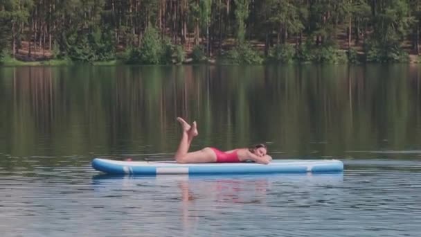 Seitenansicht einer attraktiven Frau in roter Badebekleidung, die sich auf dem Paddelbrett sonnt und den Sommer genießt - Filmmaterial, Video