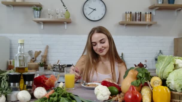 Chica encantadora comiendo brotes crudos de trigo sarraceno con nueces en la cocina con verduras y frutas frescas - Imágenes, Vídeo