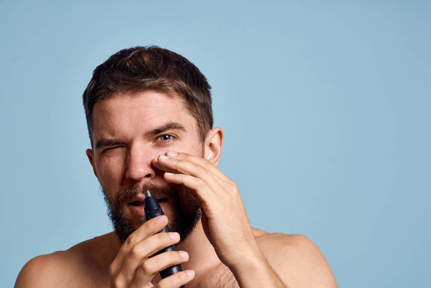 mężczyzna z gołymi ramionami usuwa higieny nosa pielęgnacja niebieskie tło - Zdjęcie, obraz