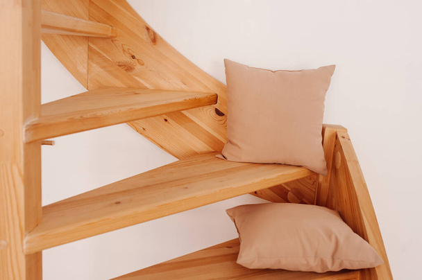 dos almohadas beige hechas de tela natural en una escalera de caracol de madera en la casa. Acogedora decoración natural para el hogar, enfoque selectivo - Foto, imagen