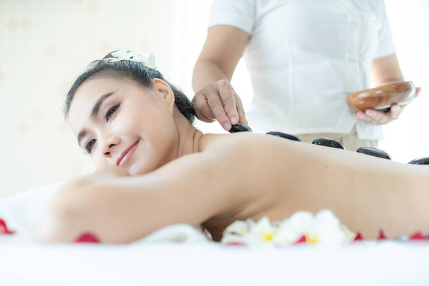 Eine Wellness-Masseurin setzt einer Asiatin einen heißen Stein auf. Liegen in einem entspannenden Massage-Spa. - Foto, Bild