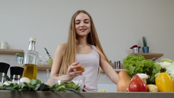 Vegane Mädchen kochen Salat mit rohem Gemüse und fügen Zitronensaft hinzu. Eine Zitrone in die Hände drücken - Filmmaterial, Video
