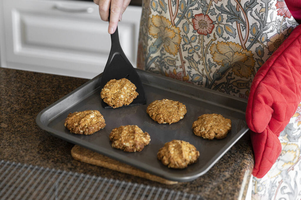 Zelfgemaakte anzac koekjes worden overgebracht naar een kookplaat. - Foto, afbeelding