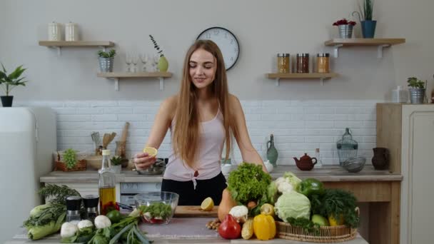 Veganistisch meisje in de keuken voegt citroensap toe aan salade met rauwe groenten. Gewichtsverlies en dieet concept - Video