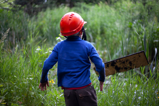 Child in the forest in an orange construction helmet. The boy's walk in an unknown place. Lost child in the mountains. The tourists forgot the boy. - Φωτογραφία, εικόνα