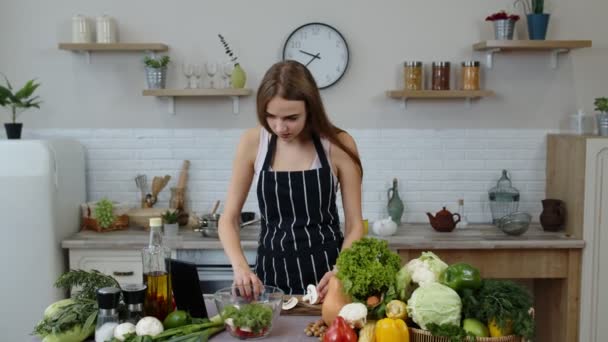 Vegan ragazza cottura insalata con verdure crude, mentre guardando su tablet digitale per ricetta online - Filmati, video