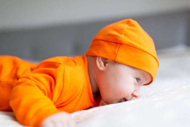 High Angle View Of Baby In Pumpkin Costume. Happy Kid two months old in orange Halloween costume on bed - Фото, изображение