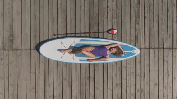 一人で木製の湖の桟橋にひっそりと横たわっているリラックスしたスポーティ女性のドリーアウトトップビューショット - 映像、動画