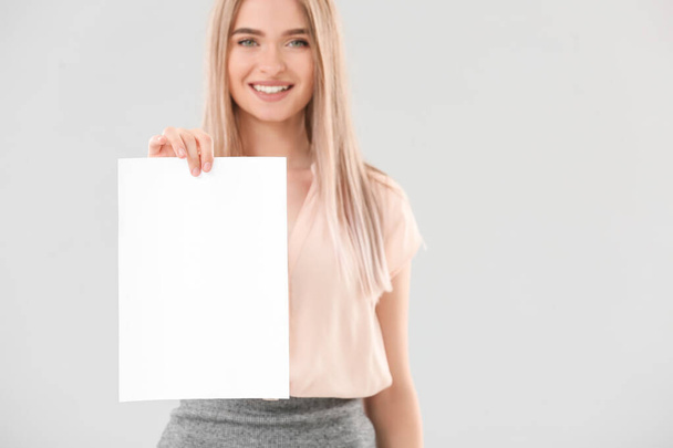 Jonge vrouw met blanco vel papier op lichte achtergrond - Foto, afbeelding