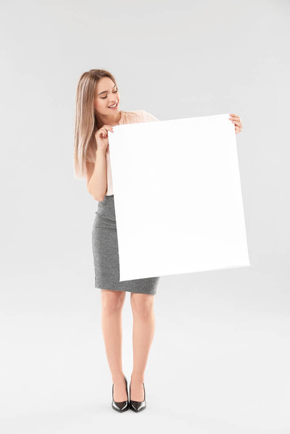 Young woman with blank paper sheet on light background - Valokuva, kuva