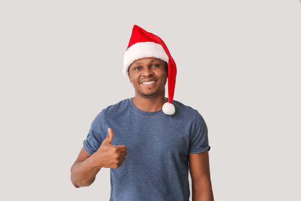 African-American man in Santa hat showing thumb-up on light background - Photo, Image