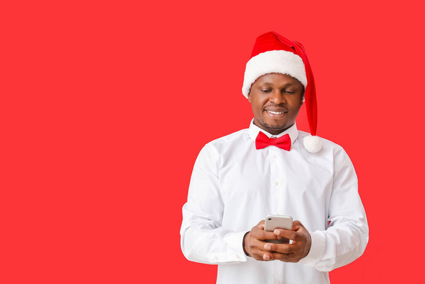 Afro-Américain dans le chapeau de Père Noël et avec téléphone portable sur fond de couleur - Photo, image