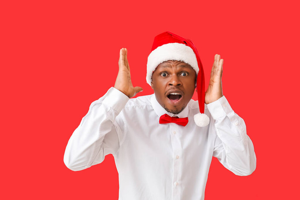 Shocked African-American man in Santa hat on color background - Photo, Image