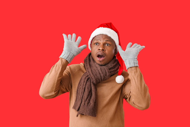 Shocked African-American man in Santa hat and gloves on color background - Foto, Imagem