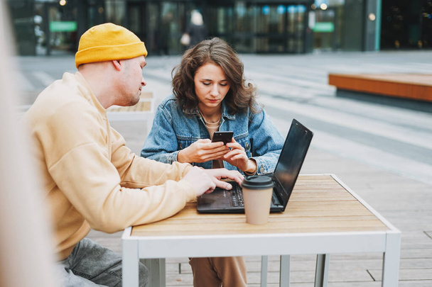 Стильная молодая пара фрилансеров, работающих на ноутбуке в уличном кафе - Фото, изображение