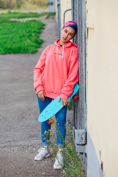 Stylish young woman with short colored hair holding blue plastic skateboard in hand. Youth concept. - Φωτογραφία, εικόνα