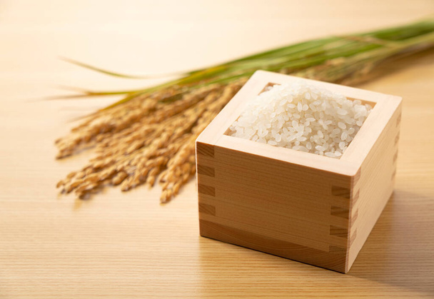 Rice and ears of rice in a Japanese Masu box set against a wooden background - Fotoğraf, Görsel